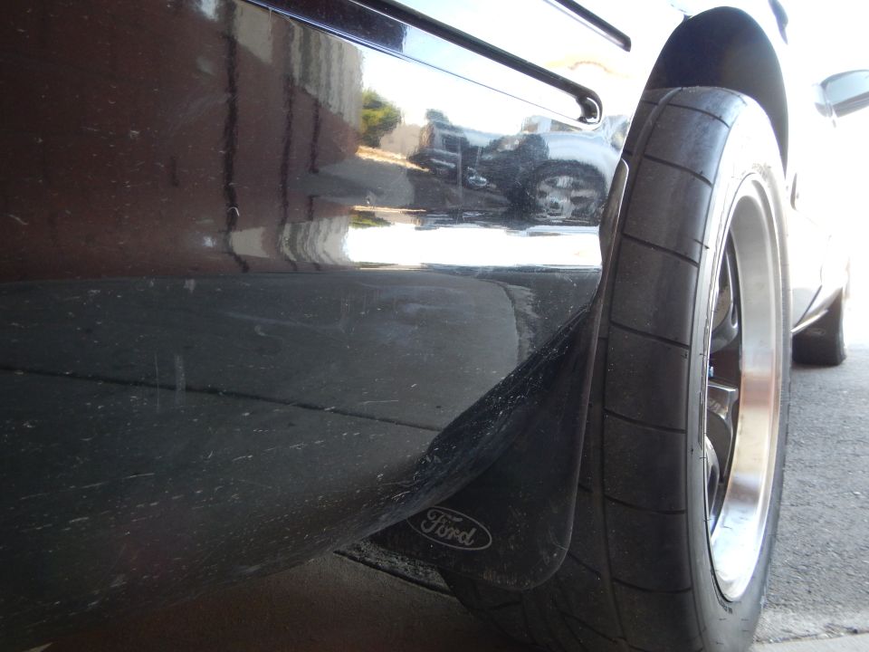 Black sedan rear wheel and Ford-branded mud flap close-up