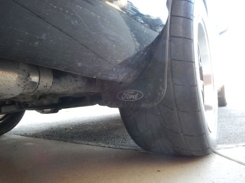 2003 Ford Crown Victoria - Low view beneath a black sedan's rear showing a Ford mud flap, wide tire and exhaust pipe.