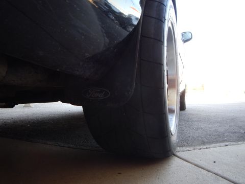 2003 Ford Crown Victoria - Low-angle view of a black sedan's rear wide tire and Ford mud flap with a side mirror reflected on the body.