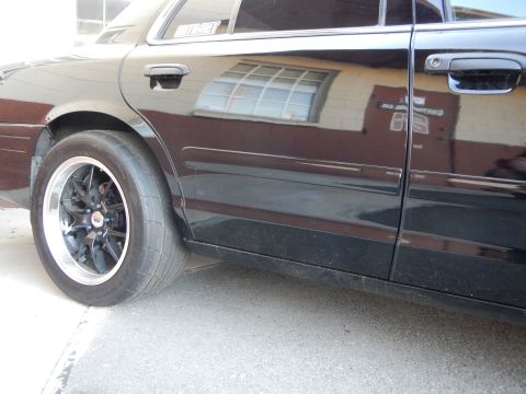 2003 Ford Crown Victoria - Side rear view of a black sedan showing a black wheel, door handle and tinted rear window.