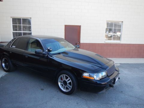2003 Ford Crown Victoria - Front three-quarter view of a black full-size sedan with a cowl-induction hood parked beside a building.