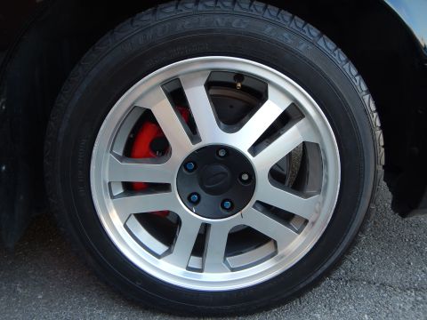 2003 Ford Crown Victoria - Detailed view of a silver seven-spoke alloy wheel with a red brake caliper on a touring-type tire.
