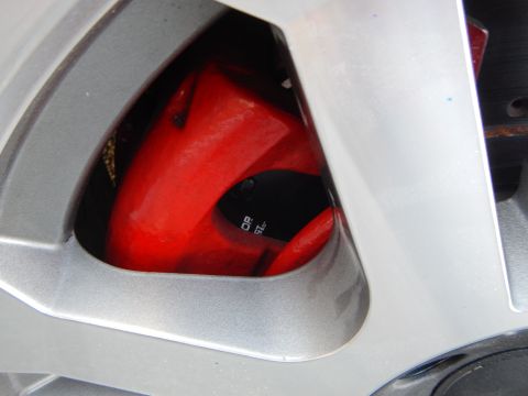 2003 Ford Crown Victoria - Macro view of a red brake caliper visible through the spokes of a silver alloy wheel.