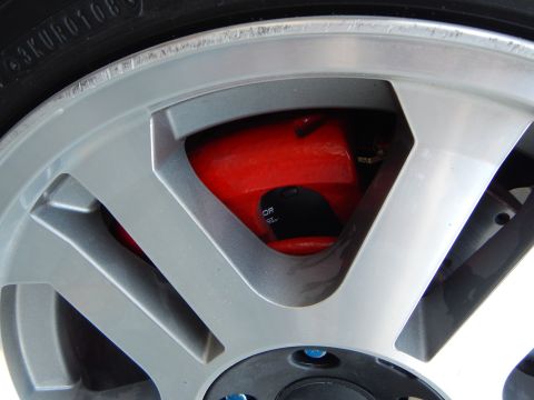 2003 Ford Crown Victoria - Close-up of a red brake caliper and rotor seen between the spokes of a silver alloy wheel.
