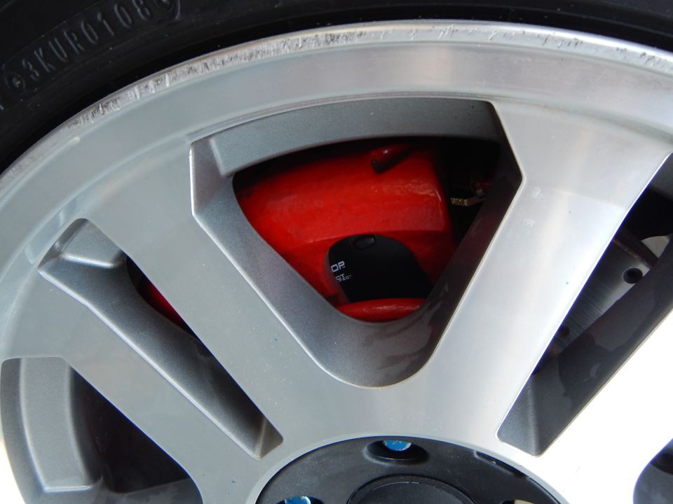 Close-up of red brake caliper and rotor behind silver alloy wheel spokes
