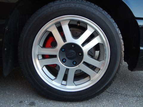 2003 Ford Crown Victoria - Close-up of a machined silver multi-spoke alloy wheel mounted on a low-profile touring tire, with a red brake caliper showing behind the sp…
