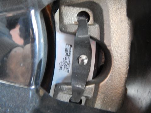 2003 Ford Crown Victoria - Close-up of a Perfect Stop Ceramic brake pad held in place by a metal retaining clip inside a brake caliper.