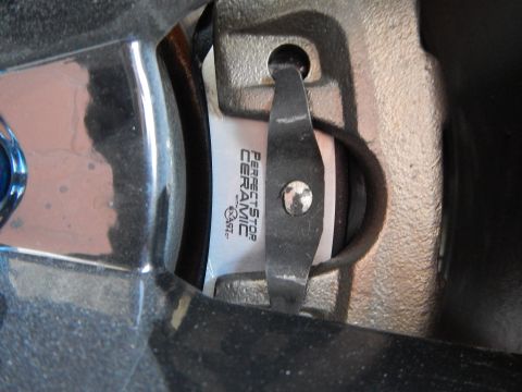 2003 Ford Crown Victoria - Perfect Stop Ceramic brake pad in its caliper, viewed past a blue-tipped lug nut through a wheel spoke.