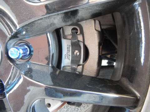 2003 Ford Crown Victoria - ceramic brake pad and caliper photographed through the spokes of a wheel, with a blue-anodized lug nut in the foreground.