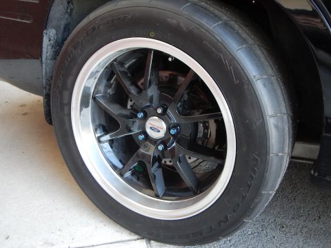 2003 Ford Crown Victoria - black alloy wheel with a polished machined lip and Ford center cap, fitted with a drag-style tire on a dark car in a garage.