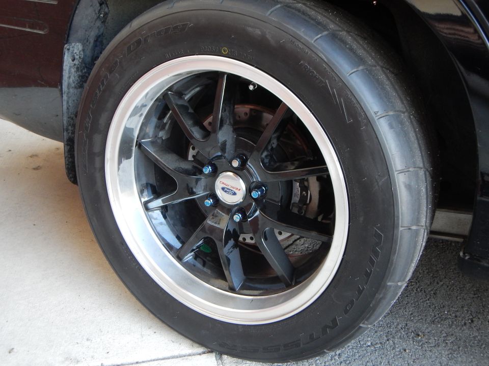 Black machined-lip alloy wheel with Ford center cap on drag-style tire in garage