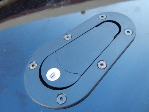 2003 Ford Crown Victoria - Angled view of a black oval flush-mount latch with a metal pull tab set into a blue painted body panel.