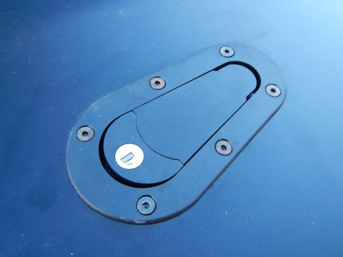 2003 Ford Crown Victoria - black oval recessed latch with a small pull tab, mounted in a dark blue painted body panel.