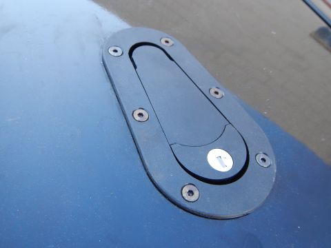 2003 Ford Crown Victoria - black oval flush-mount latch with a recessed pull tab, installed in a glossy blue body panel in sunlight.