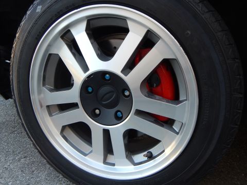 2003 Ford Crown Victoria - machined silver multi-spoke alloy wheel with blue lug nuts and a red brake caliper, mounted on a low-profile tire.