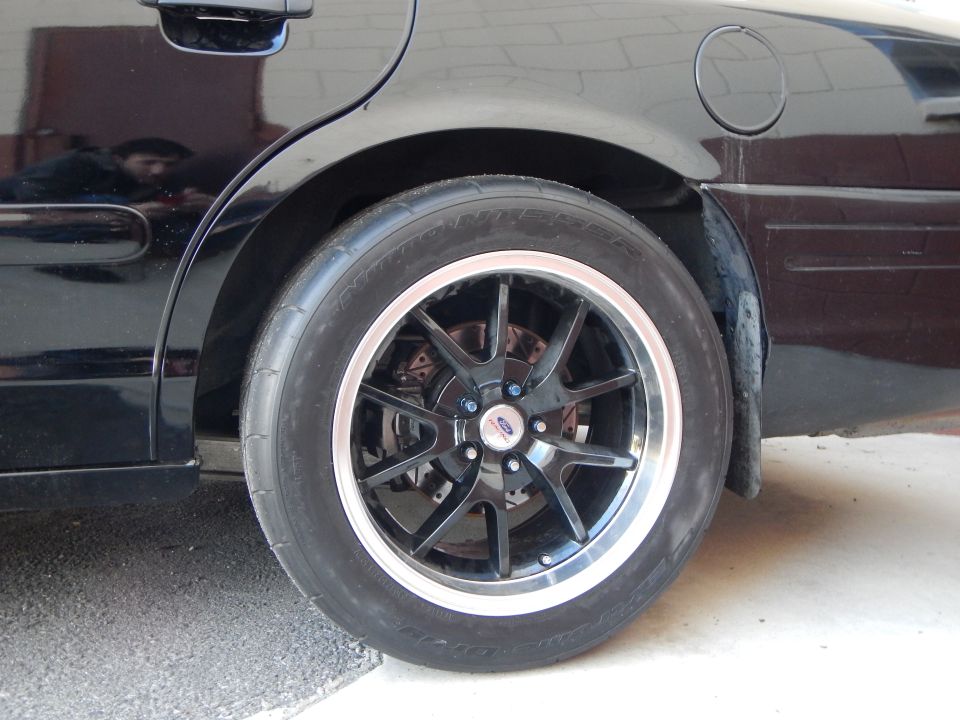 Black car rear wheel with black machined-lip alloy and drag tire in garage