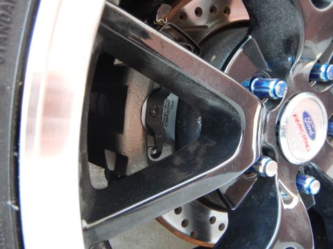 2003 Ford Crown Victoria - chrome Ford Racing center cap with blue lug nuts on a black wheel, with a drilled brake rotor and caliper visible behind.