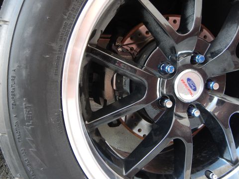 2003 Ford Crown Victoria - black multi-spoke alloy wheel with a Ford Racing center cap, blue lug nuts and a drilled rotor, on a treaded tire.