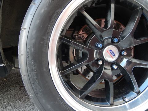2003 Ford Crown Victoria - black alloy wheel with a machined lip, Ford Racing center cap and blue lug nuts, mounted on a treaded tire.