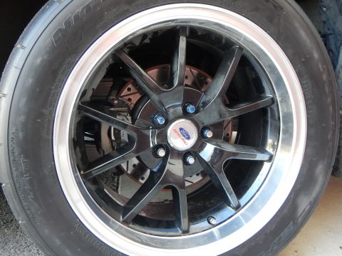 2003 Ford Crown Victoria - black multi-spoke alloy wheel with a Ford center cap and polished lip, fitted on a Nitto tire in a garage.