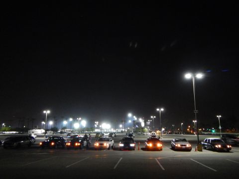 2003 Ford Crown Victoria - row of sedans in a dark parking lot at night with amber parking lights lit and faint cloud streaks overhead.
