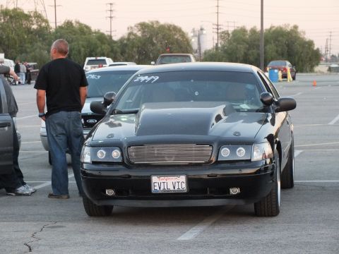 2003 Ford Crown Victoria - Front view of a lowered black full-size sedan with a billet grille, halo headlights, and a California plate reading EVIL VIC.