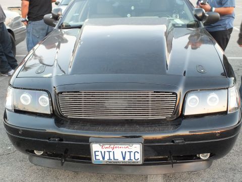 2003 Ford Crown Victoria - Front end of a glossy black Ford Crown Victoria with a billet grille, halo headlights, and a California EVIL VIC license plate.