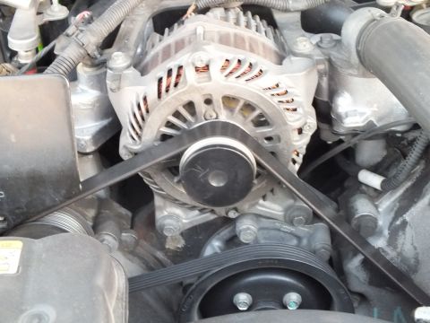 2003 Ford Crown Victoria - Tight close-up of an alternator with visible copper windings, driven by a serpentine belt over the crank and accessory pulleys.