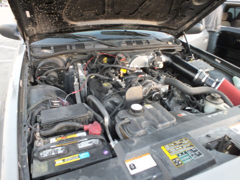 2003 Ford Crown Victoria - Overhead view of an open engine bay with the battery at left, central intake plenum and a red aftermarket air filter on the right side.