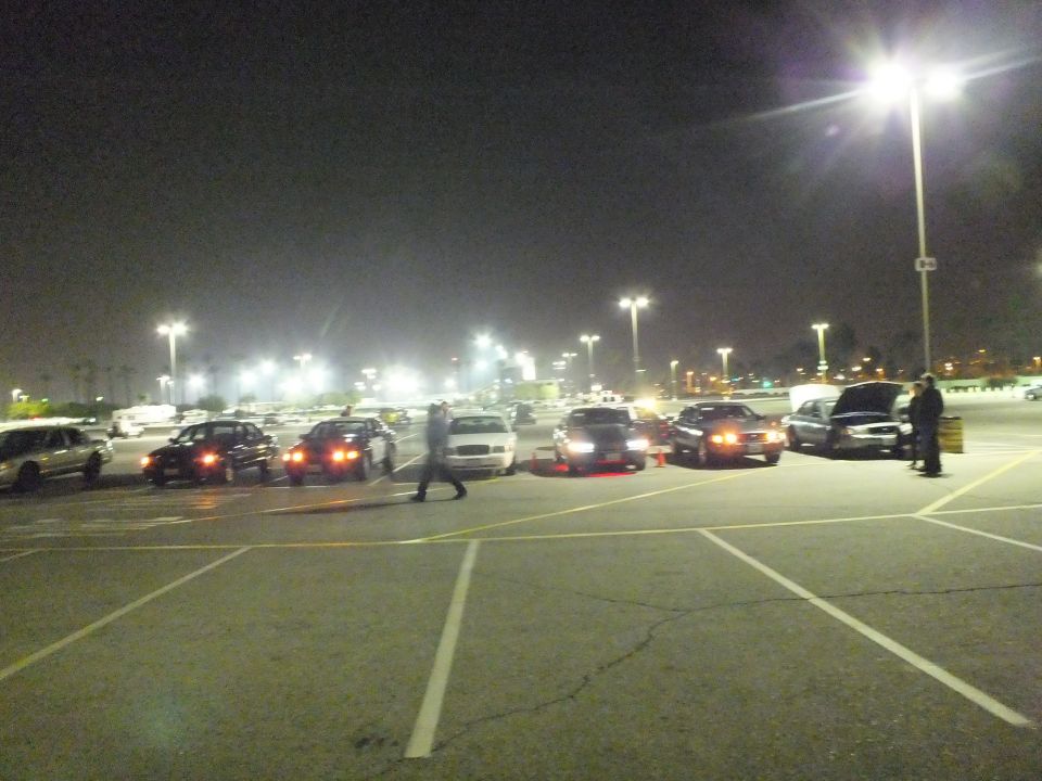 Nighttime lot with parked cars, a person walking and another at an open hood