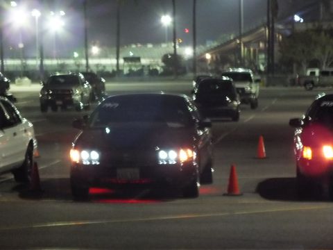 2003 Ford Crown Victoria - Front view of a dark sedan with bright HID headlights and red underglow at night, flanked by orange traffic cones in a lot.
