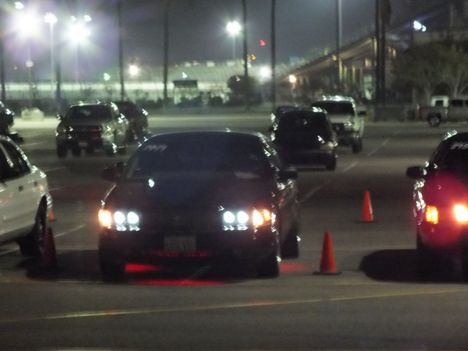 Front of a dark sedan with HID headlights between traffic cones at night