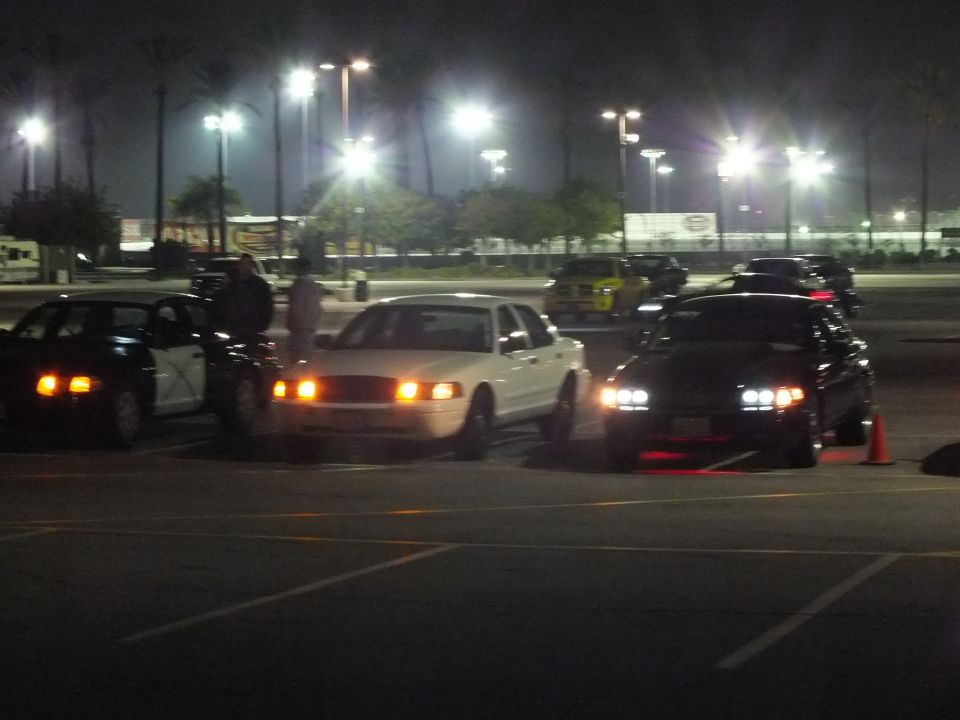 White sedan flanked by dark sedans at night in a parking lot