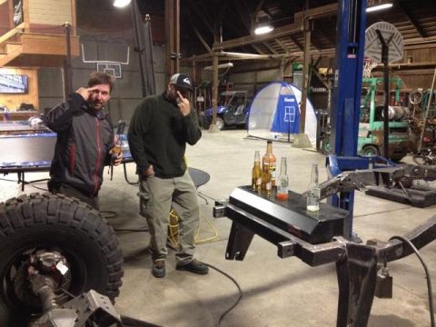1985 Jeep CJ7 - Two men stand in a garage with a large tire and vehicle frame in the foreground.