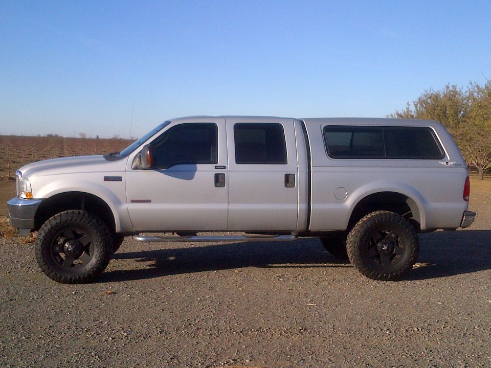 Silver crew cab pickup truck with a camper shell, lifted with large tires