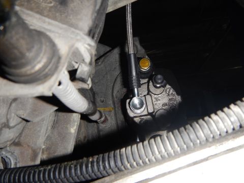 2003 Ford Crown Victoria - Close-up underbody shot of a cast metal component with a braided stainless brake line attached by a banjo bolt fitting.