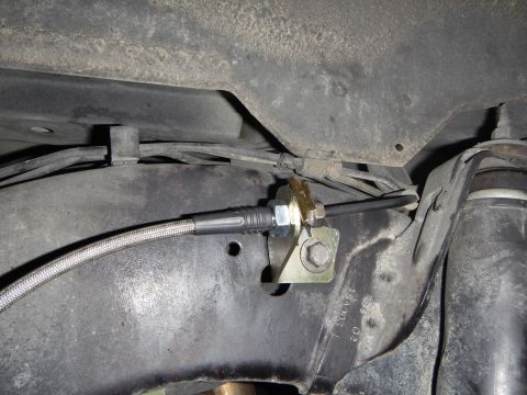2003 Ford Crown Victoria - Underbody close-up of a yellow-zinc bracket bolted to the frame holding a braided stainless brake line in place with a hex nut.