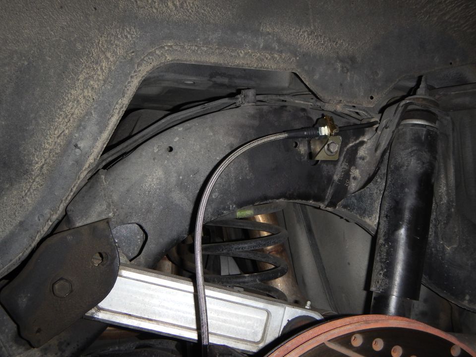 Rear suspension underside showing coil spring, control arm and routed brake line