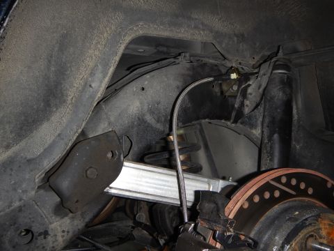 2003 Ford Crown Victoria - Underbody shot of a rear suspension showing the coil spring, lower control arm, rusty brake rotor and a routed braided brake line.