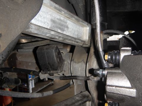 2003 Ford Crown Victoria - Underbody close-up showing a rubber suspension bushing, a metal subframe, and a brake caliper fed by a braided stainless brake line.