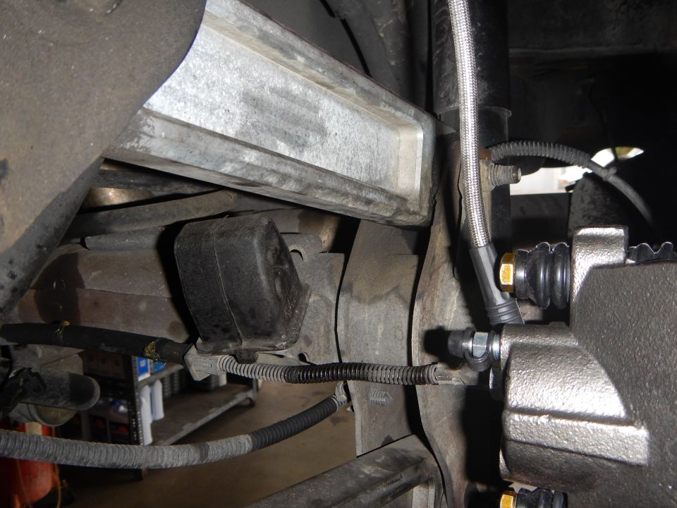 Underbody view of a rubber suspension bushing and brake caliper with braided line