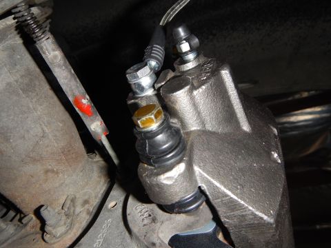 2003 Ford Crown Victoria - underbody close-up of a brake caliper with a banjo bolt fitting and rubber boot, alongside a parking-brake cable.