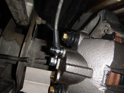 2003 Ford Crown Victoria - brake caliper fitted with a braided stainless-steel brake line and gold banjo bolt, viewed from beneath the vehicle.