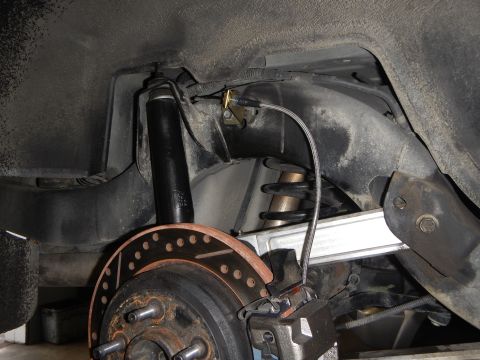 2003 Ford Crown Victoria - underbody shot showing a rear shock absorber, coil spring, control arm and a cross-drilled brake rotor on the hub.