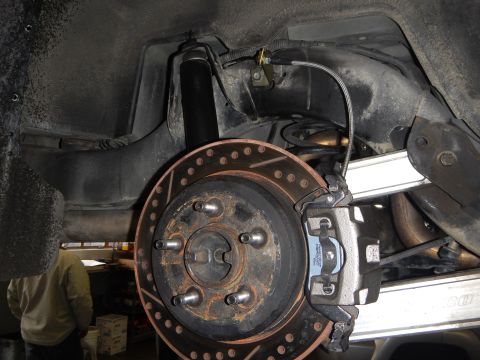 2003 Ford Crown Victoria - underbody view of a cross-drilled, slotted brake rotor with caliper, exposed wheel hub and five lug studs.