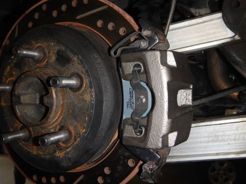 2003 Ford Crown Victoria - close-up of a cast brake caliper clamped over a drilled-and-slotted rotor, with a brake pad and lug studs visible.