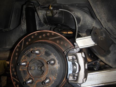2003 Ford Crown Victoria - underbody view of a drilled rear brake rotor with caliper, shock absorber and sensor wiring on the suspension.