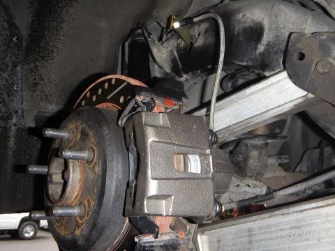 2003 Ford Crown Victoria - underbody view of an exposed wheel hub with lug studs, a brake caliper and rotor amid suspension components.