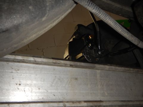 2003 Ford Crown Victoria - dim underbody view of a brake caliper and line seen above an aluminum subframe brace stamped METCO.