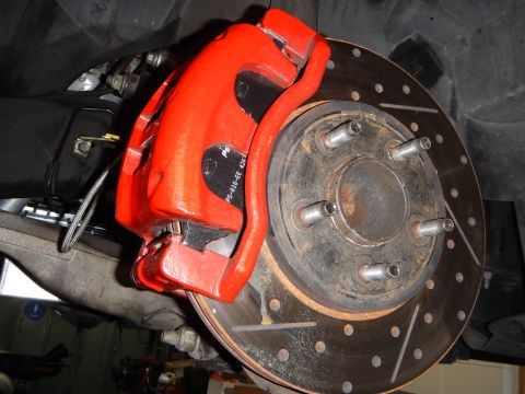 2003 Ford Crown Victoria - bright red painted brake caliper clamped over a cross-drilled and slotted brake rotor, viewed from underneath.